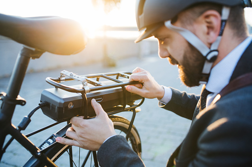 Hipster businessman commuter setting up electric bicycle when traveling home from work in city